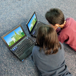 chłopcy leżący na dywanie przed laptopami